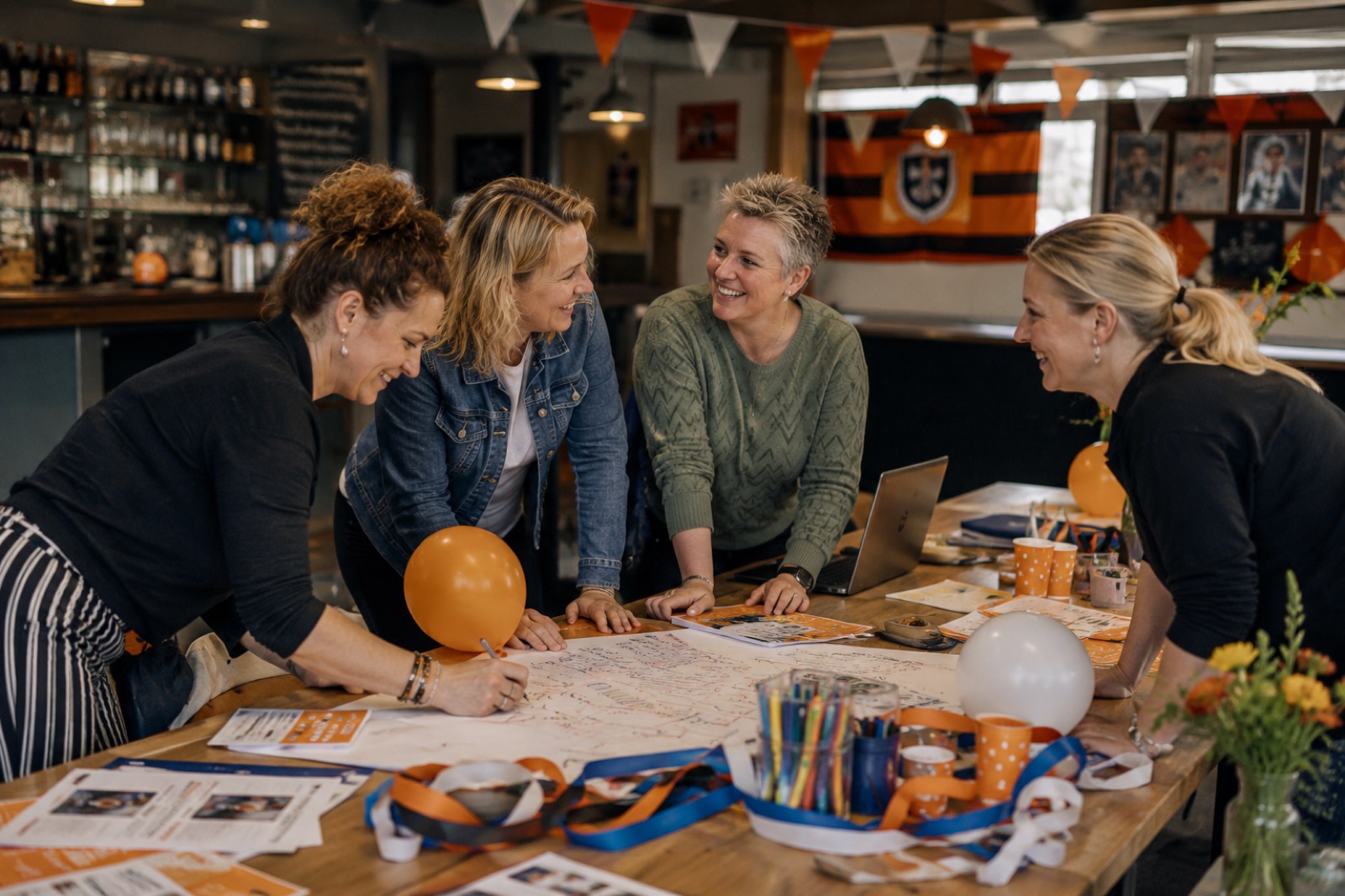Vier lachende mensen schrijven samen op een groot vel papier tussen ballonnen en slingers