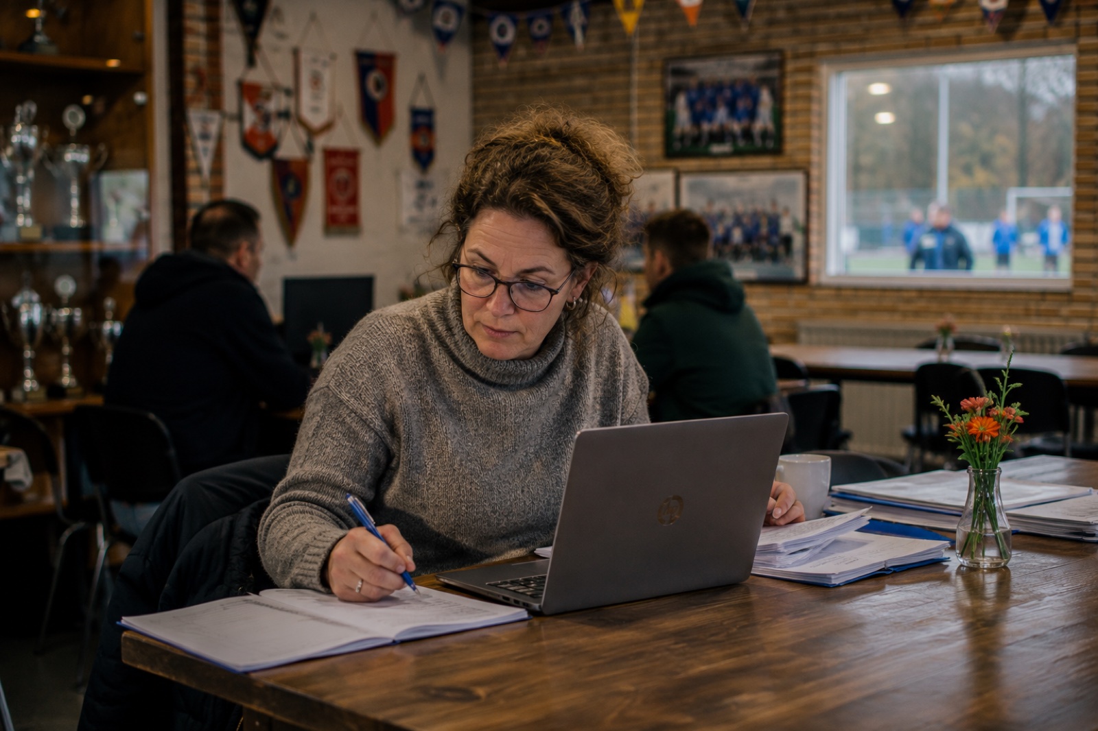Iemand schrijft aantekeningen naast een opengeklapte laptop tussen vaantjes en bekers